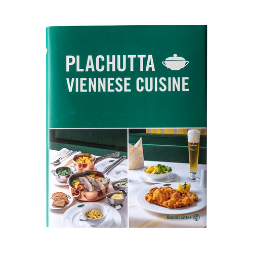 Breaded schnitzel with a lemon wedge on a white plate, with a fork and a side dish in the background.